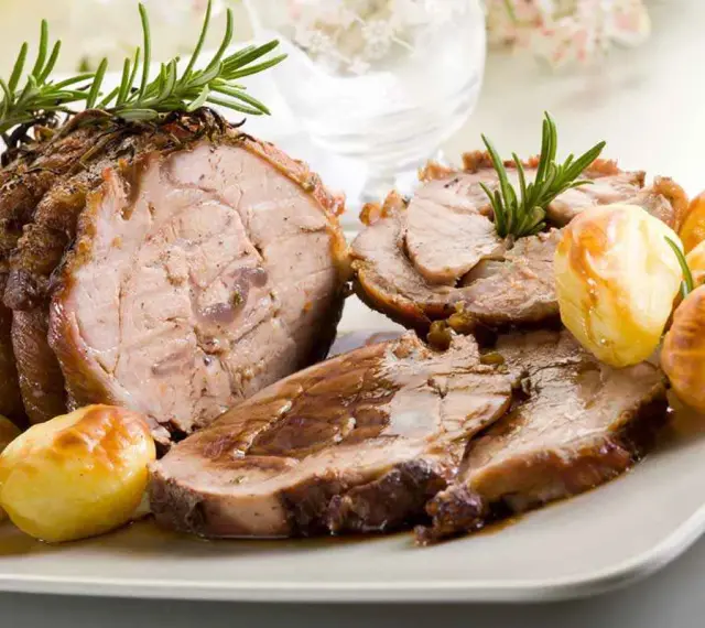 Succulento arrosto di vitello affettato, guarnito con rosmarino e accompagnato da patate arrosto dorate.