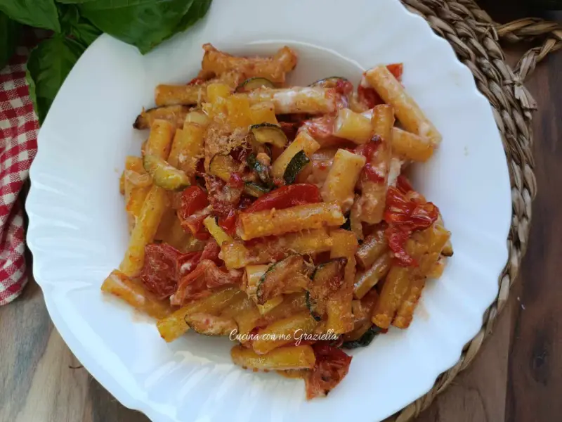 Piatto di pasta con zucchine e pomodorini, condita con formaggio grattugiato e basilico fresco.