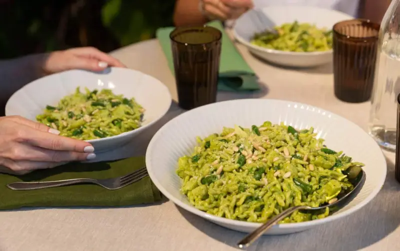 Due piatti di trofie al pesto, condite con fagiolini e pinoli, pronte per essere gustate.